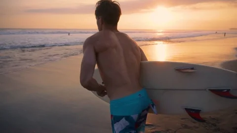Young surfer holding board, running to go in the water at amazing golden light Stock Footage