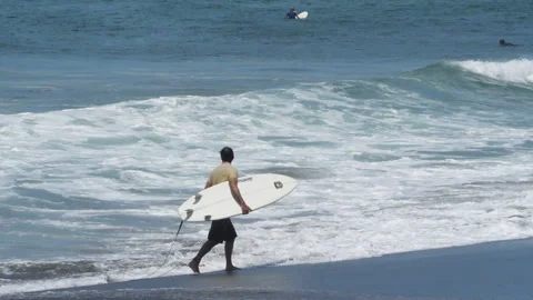 Young surfer walking on the beach with his surfboard under his arm Stock Footage 100089239