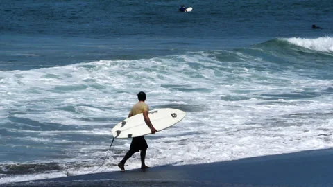 Young surfer walking on the beach with his surfboard under his arm Stock Footage 100089244