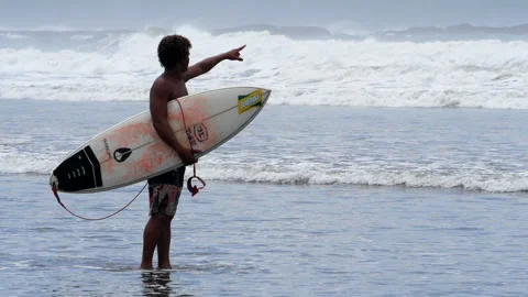 Young surfer walking on the beach with his surfboard under his arm Stock Footage 100089469