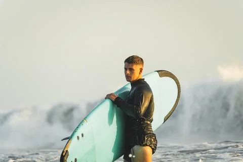 Young surfer in wetsuit looking focused with a wave behind him Stock Photos