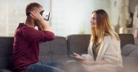 Young sweet couple on couch playing with VR headset and tablet Stock Footage 78025659