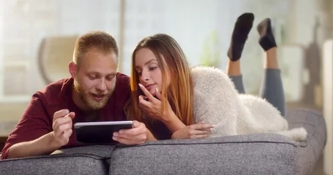 Young sweet couple lying on a couch and order something on a tablet Stock Footage 78036293