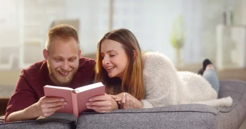 Young sweet couple lying on a couch and reading a a funny book Stock Footage 78036760