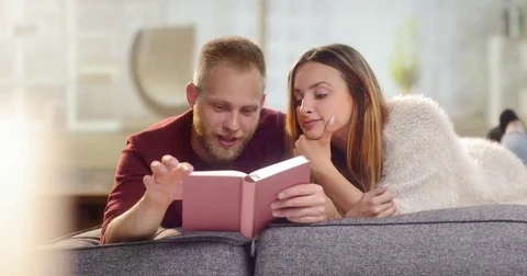 Young sweet couple lying on a couch and reading a book Stock-Footage 78037496