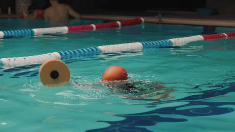 A young swimmer is seen practicing in swimming pool, wearing an orange swim cap Stock Footage 283728404