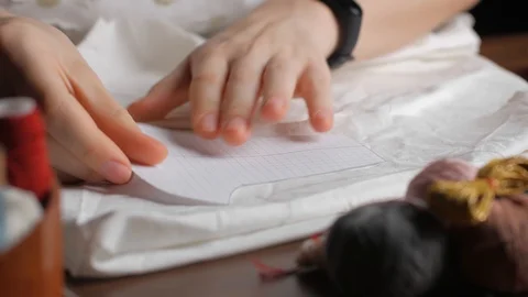 Young tailor uses red pencil to transfer patterns on white tissue. Close up w Video stock 128363355