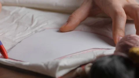 Young tailor uses red pencil to transfer patterns on white tissue. Close up w Stock-Footage 128363388