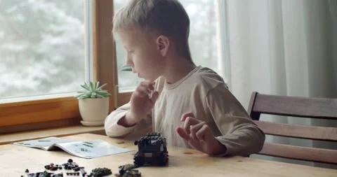 Young talented boy sitting at table engineering car at home by window slow Stock Footage 146570056