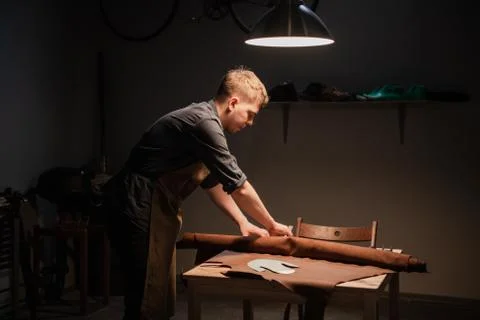 A young talented shoemaker in the workshop is engaged in manual production of Stock Photos