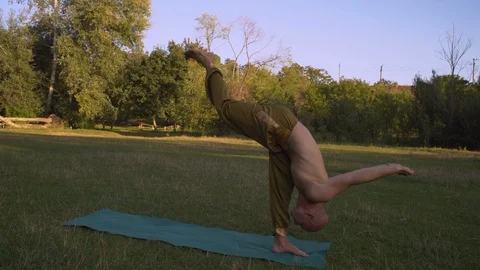 Young Tanned Guy Performs Yoga Asanas In the morning on the Glade in the City Stock Footage 85843996