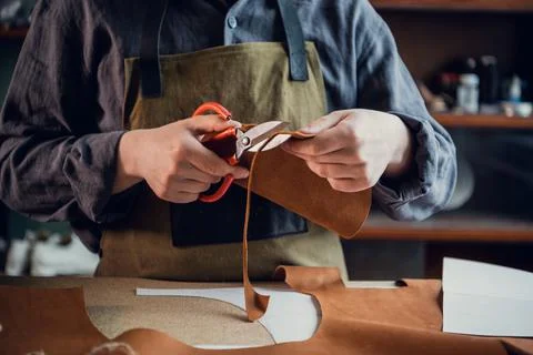 A young tanner in his workshop at the table cuts out leather elements of shoes Foto stock