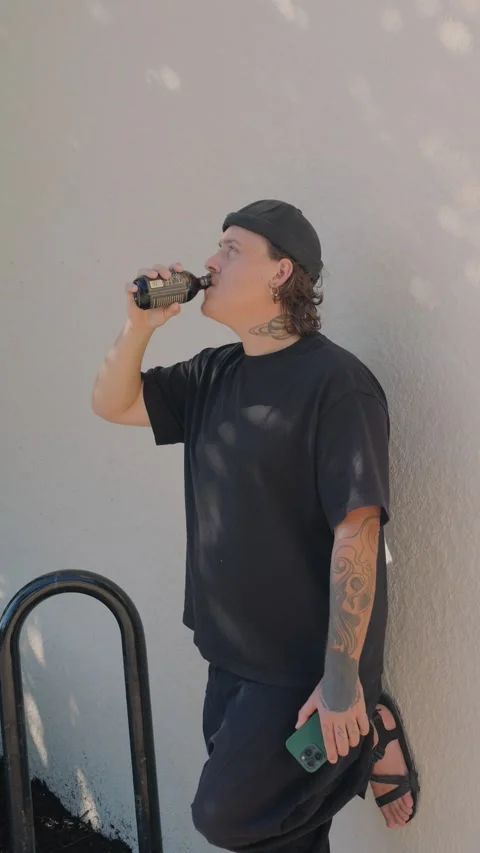 Young tattooed man in black  drinking from bottled coffee while... Vidéo 323327978