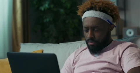 Young teacher of African appearance is preparing for lecture. He is sitting on Stock Footage 218099253
