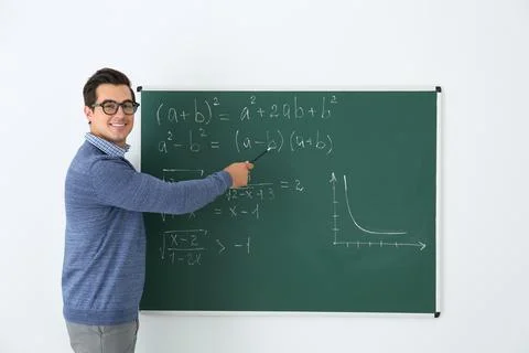 Young teacher explaining math formulas written on chalkboard in classroom Stock Photos