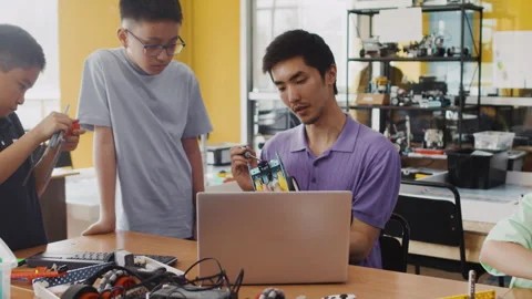 Young teacher explains to children in a class at a robotics lesson how the Stock Footage 242170374
