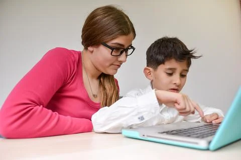 Young teacher helping elementary student with laptop in classroom Stock Photos