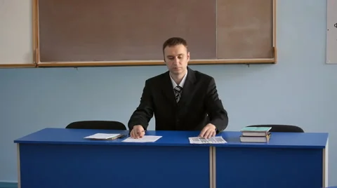 The young teacher in the jacket checking exam tests in the classroom Stock Footage 64216399
