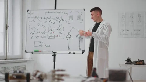 Young teacher in lab coat talking and showing mathematical formula on whiteboard Video stock 83748929