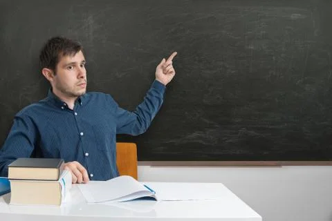 Young teacher is pointing on empty blackboard with finger. Stock-Fotos
