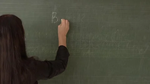 A young teacher writes on a blackboard back to school, turns and takes off her Stock Footage 138399320