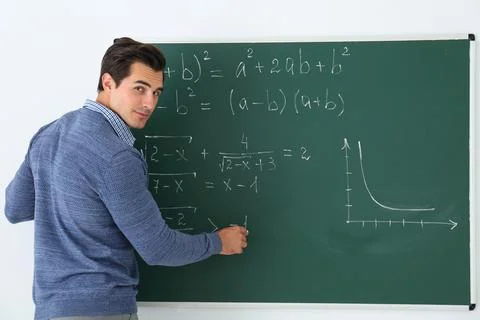 Young teacher writing math formulas on chalkboard in classroom Stock Photos