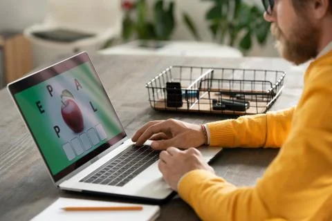 Young teacher in yellow pullover making online task for his students by table Stock Photos