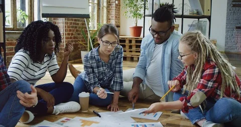Young team of multiethnical young workers of the company sitting ob the floor in Stock Footage 100996065