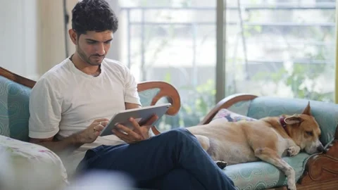A young tech savvy male using a tablet next to a sleeping pet dog Stock Footage 306291506