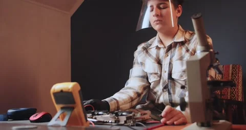 A young technician examines a computer video card. Teenager in protective mask Stock Footage 265158887