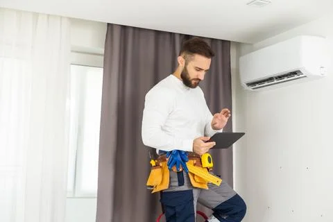 Young Technician using digital tablet and pen checking air conditioner in house Stock Photos