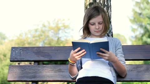 Young teenage girl reading book outdoors... | Stock Video | Pond5