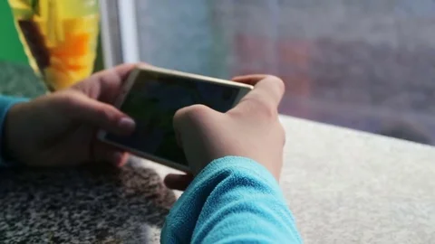Young teenager playing game on smartphone in cafe next to lemon tea with Stock Footage