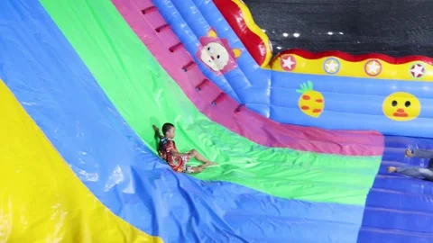 Young Thai Boy Sliding Down Large Colorful Inflatable Slide at Night Stock Footage 327828342