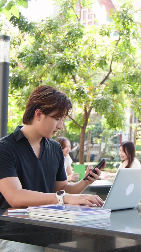 Young Thai Male Student Using Laptop and Smartphone on University Campus Stock Footage 329461653