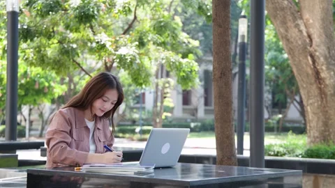 Young Thai University Student Studying with Laptop and Textbook Outdoors Stock Footage 337600488