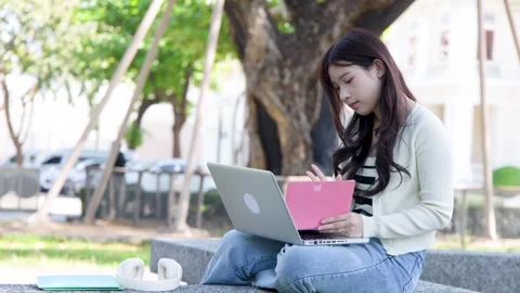 Young Thai University Student Using Laptop and Notebook in Outdoor Campus Park Stock Footage 334165533