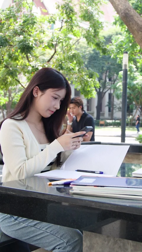 Young Thai University Student Using Smartphone While Studying Outdoors Vídeo Stock 334713162
