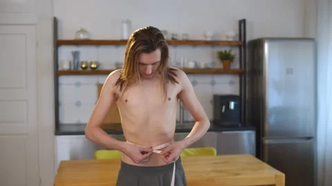 Young thin shirtless man measuring waist with tape at home Stock Footage 145844663