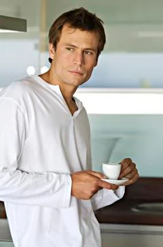 Young thinking man in kitchen, holding coffee cup Stock Photos