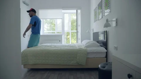 Young tired man falling on the bed holding racket after playing tennis in a Video stock 113442781