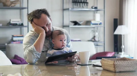 Young tired man with small kid on knee sleeping by table in the morning HD Stock Footage 57538899