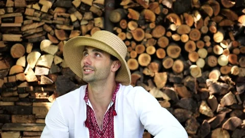 Young tired man in vyshyvanka sitting after hard work near woodshed. Ukrainian g Stock Footage 328852353