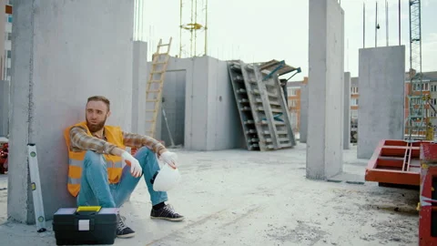 Young tired man worker sitting and takes off white hardhat Stock Footage 247769663