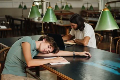 Young tired student with notepad sleeping on desk during study in library of Stock Photos