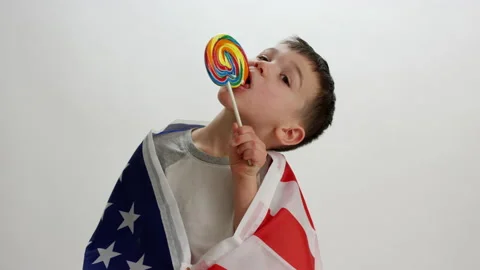 Young toddler bites into lollipop while wrapped in american flag - American c Stock Footage 142297431