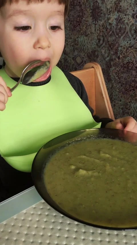 Young toddler boy witth silicone bib eating alone soup with spoon. Stock Footage 165239248