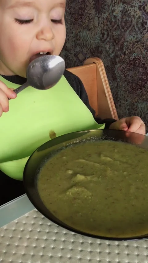 Young toddler boy witth silicone bib eating alone soup with spoon. Stock Footage 165239307
