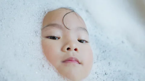 Young toddler's face emerges from thick bath foam Stock Footage 339047547