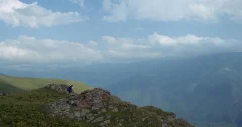 A young tourist in a cap with a backpack climbs on a rock on the background of a Stock Footage 145861735